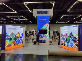 RENTAL: Custom Island Design with 16 Ft High Square Storage Tower with Lightbox, (4) 84 x 96 Double-Sided Lightbox Kiosks, (10) Large Monitor Mounts, (10) Monitors, (5) RE-1207 Large Rectangular Counters, 10 x 10 Square Hanging Sign Attached to Top of Tow