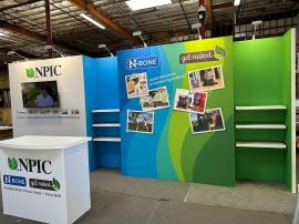 RENTAL: Inline Design with Gravitee Panel System Backwall, (6) 28" Wide x 10" Deep White Laminated Shelves, Large Monitor Mount, 43" Monitor, (6) LED Arm Lights, RE-1558 Gravitee Reception Counter, SEG Fabric Graphics -- View 3